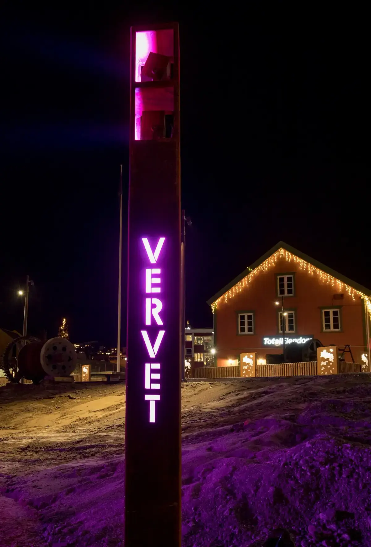Opplyst søyle med teksten Vervet om natten, med et opplyst bygg i bakgrunnen